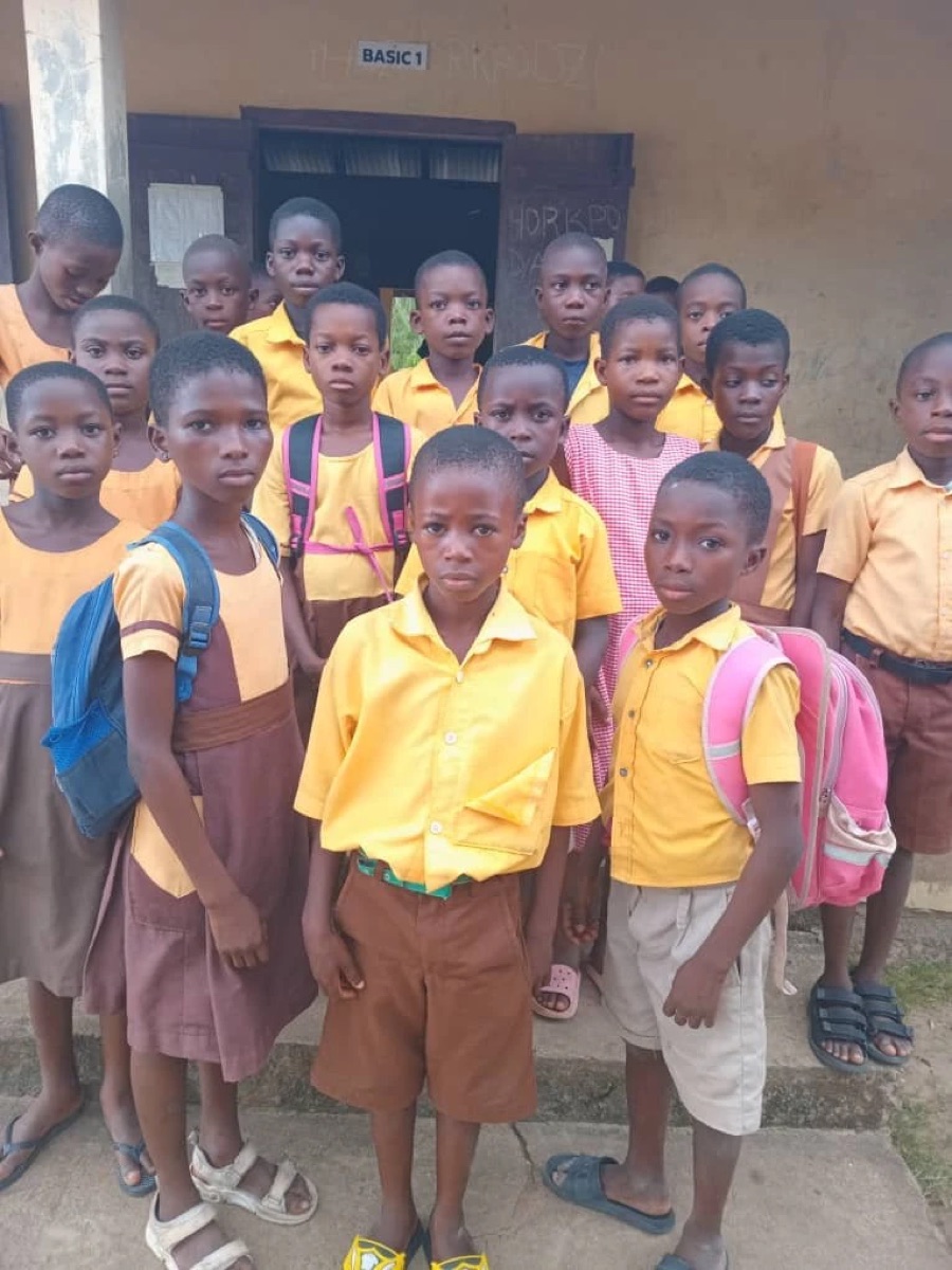Basic 1 students at Dadome DA Basic School in yellow and brown uniforms, some wearing backpacks
