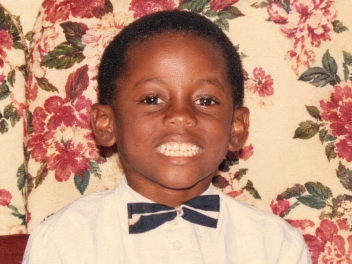Godwill as a young boy in a white shirt and bow tie, smiling