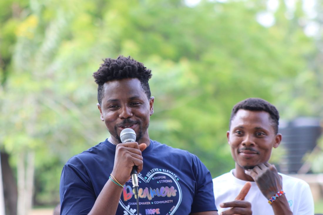 A Dreamers Wish changemaker speaking into a microphone at a community gathering in Ghana