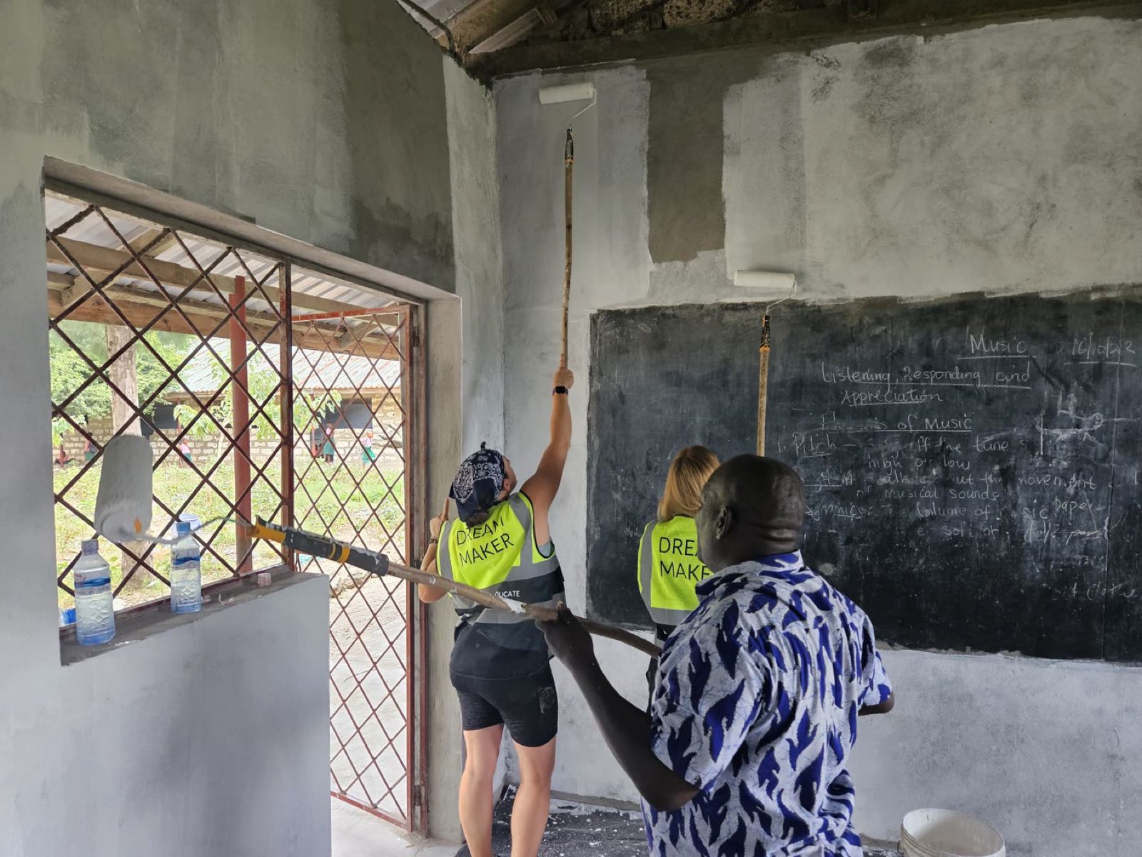 Before: bare grey classroom walls as volunteers begin painting at Mijomboni Primary