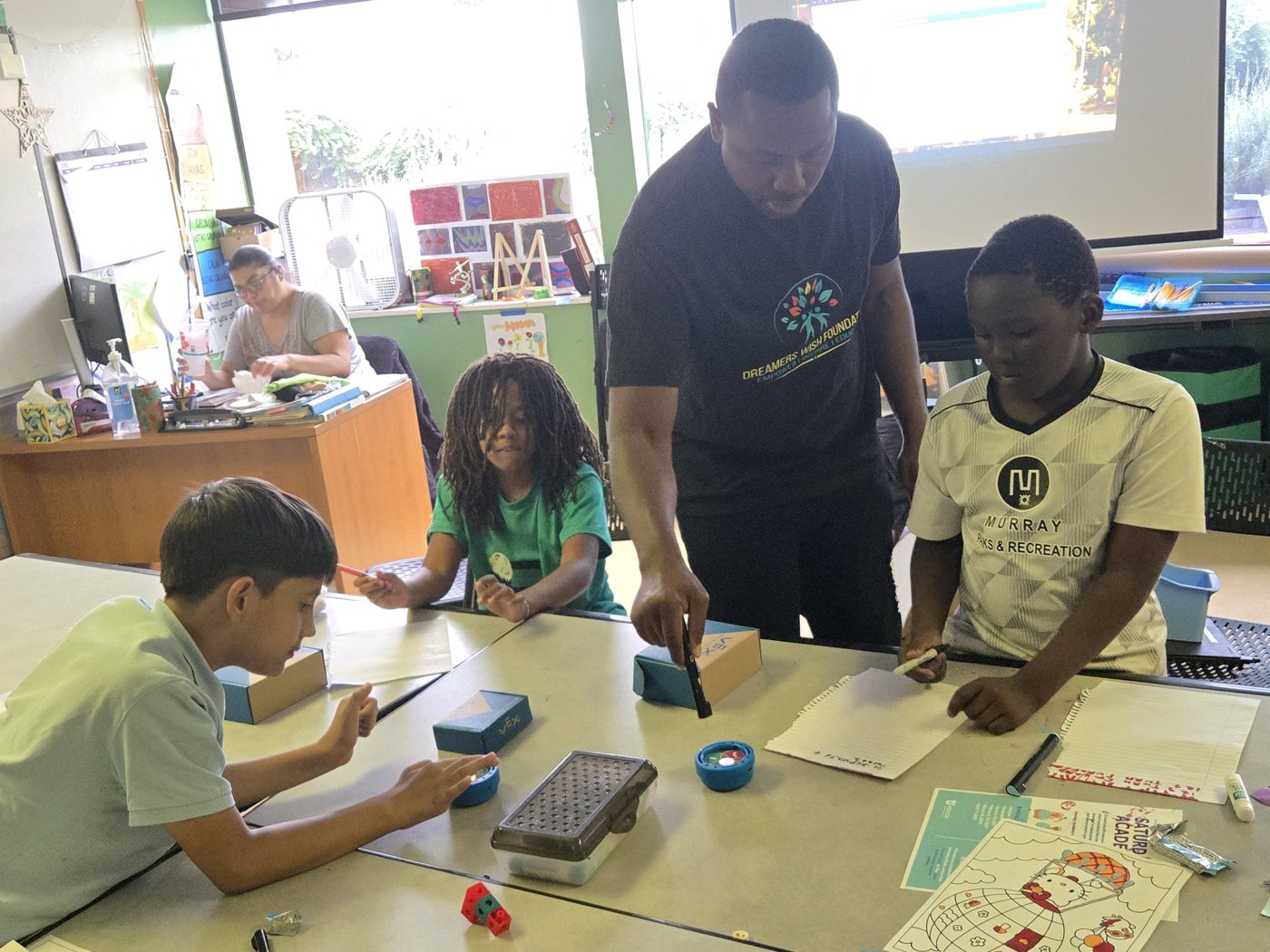 Students smiling and building together in a Dreamers Wish robotics class at the Hartland Partnership Center
